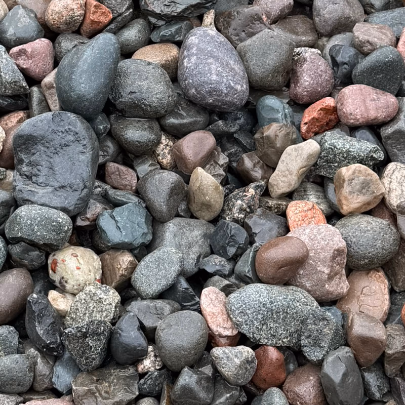 Close-up of multicolored smooth pebbles and small stones in gray, black, red, pink, and beige hues.